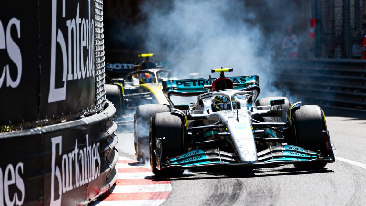 F1摩纳哥大奖赛隧道出口处一辆赛车在弯道外侧完成精彩超车，轮胎与地面摩擦产生烟雾，前后两车距离仅数十厘米，赛道旁护栏上广告牌清晰可见